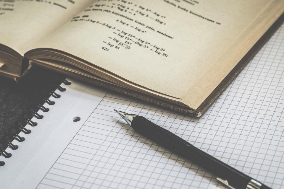 Handwritten math equation on graph paper next to a pencil and notebook