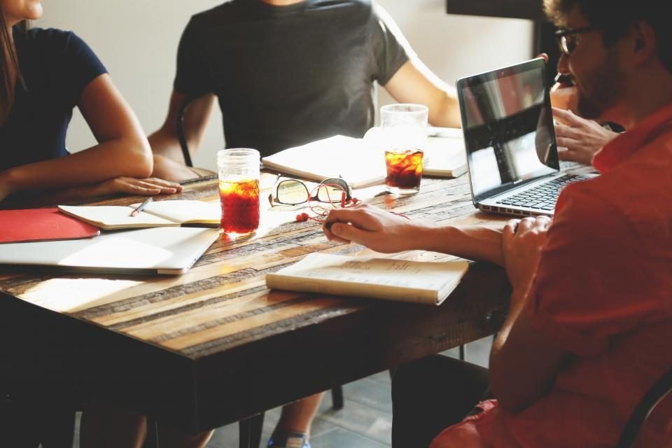 Team of coworkers around a table taking notes on laptops and notepads during a meeting